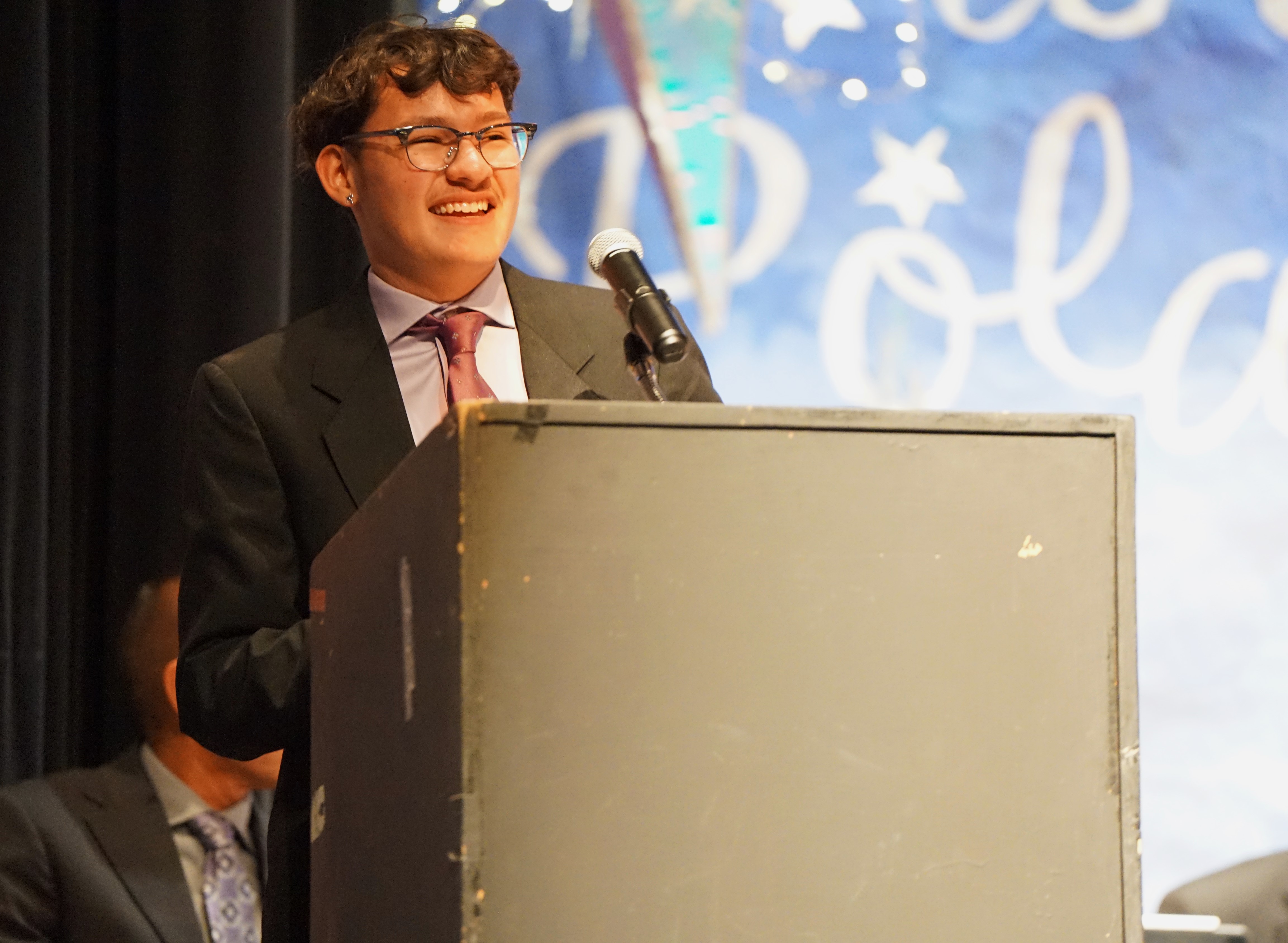 A boy in glasses smiles behind the podium