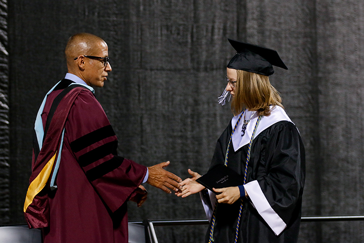 Dr. Trujillo shakes the hand of a girl in a black cap and gown