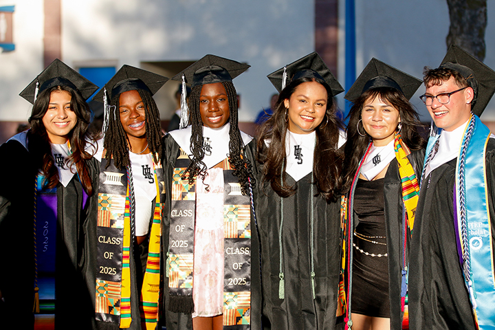 A group of graduates smile in their caps and gowns