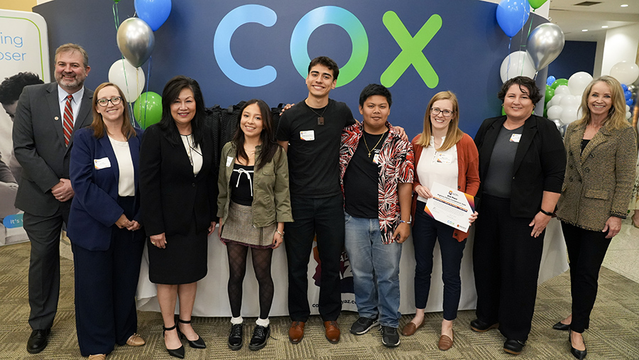 A group of students and teachers in front of a Cox banner with balloons