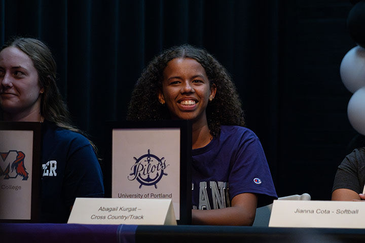 A teen girl smiles with her letter of intent from University of Portland