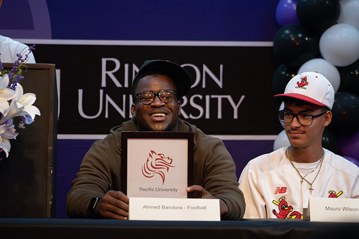 A teen boy smiles with his letter of intent from Pacific University