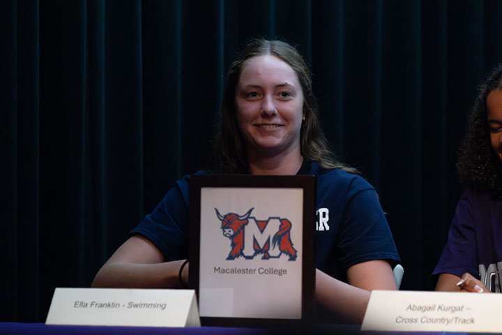 A teen girl smiles with her letter of intent from Macalester College