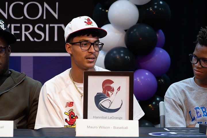A teen boy smiles with his letter of intent from Hannibal LaGrange University