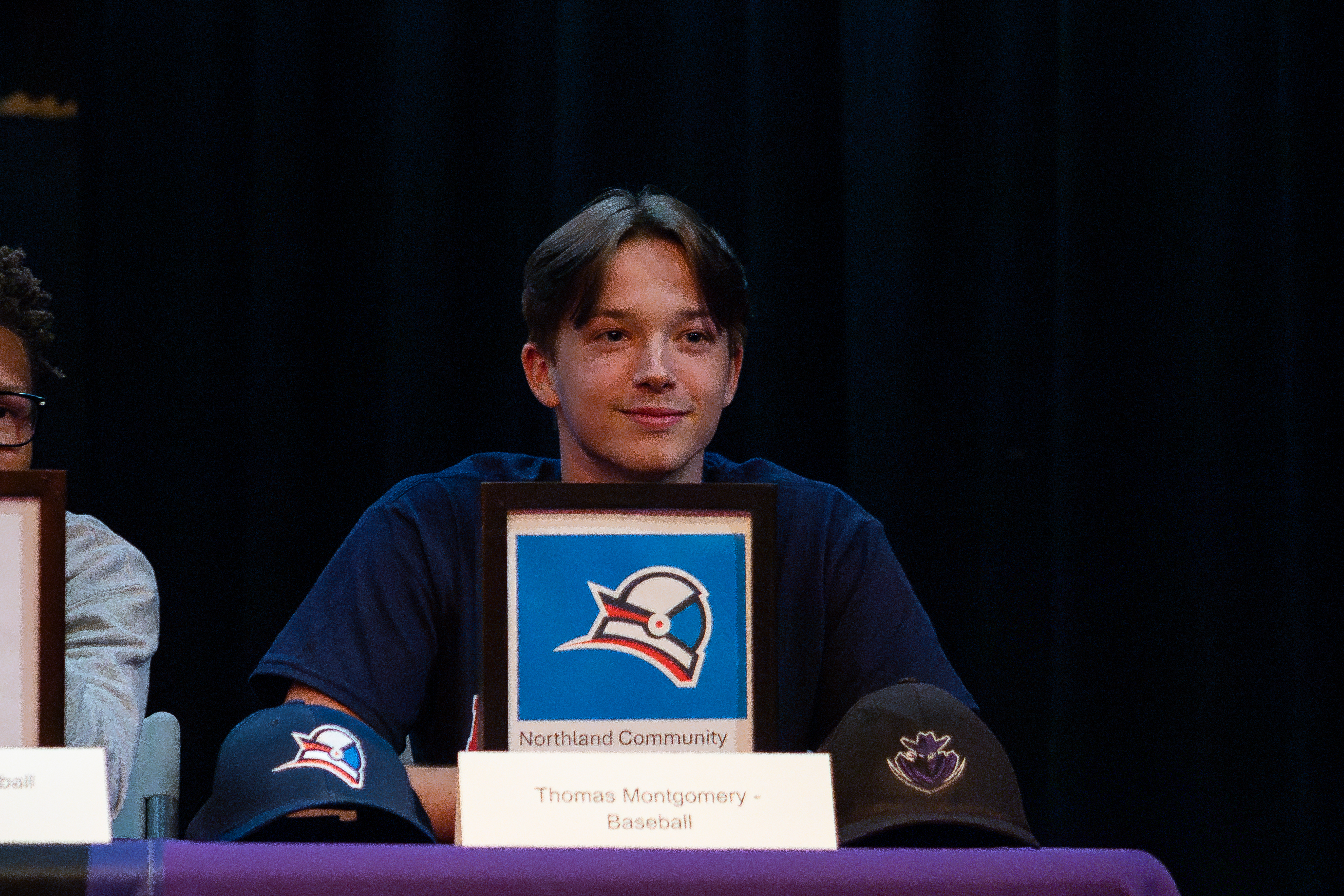 A teen boy smiles with his letter of intent from Northland Community and Technical College