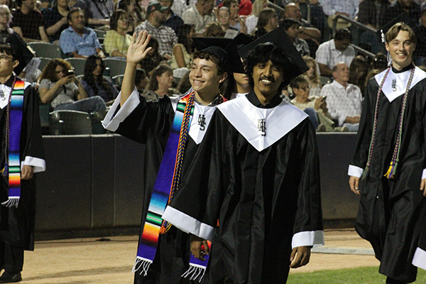 Two teen boys smile as they walk in during their graduation