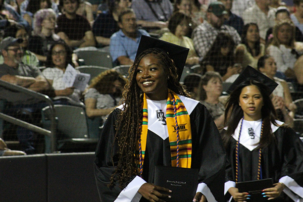 A teen girl smiles as she walks in during her graduation ceremony