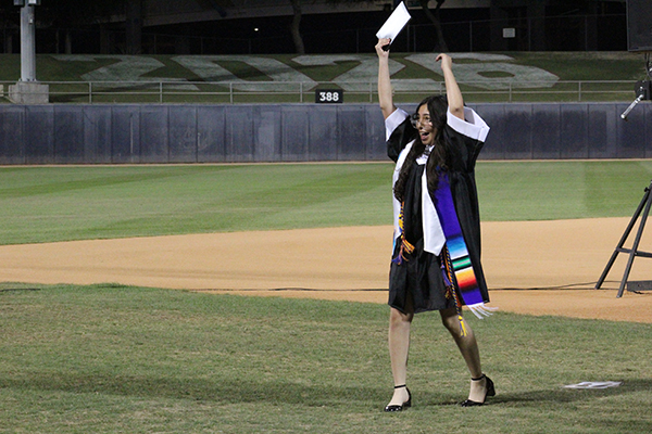A graduate raises her arms with joy as she walks across the field during the ceremony