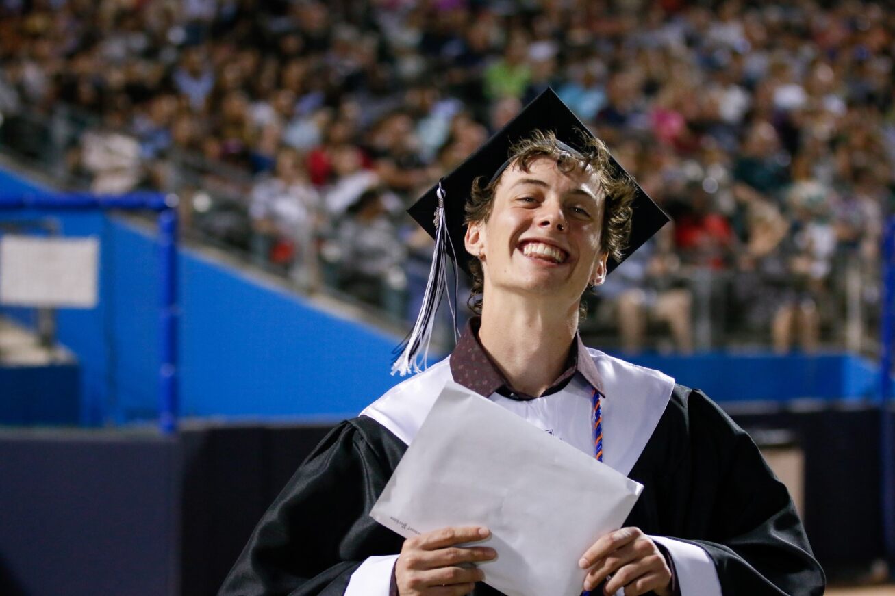 A UHS grad smiles big as he holds his diploma