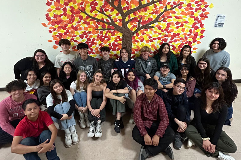 Student Council Members sit in front of tree mural
